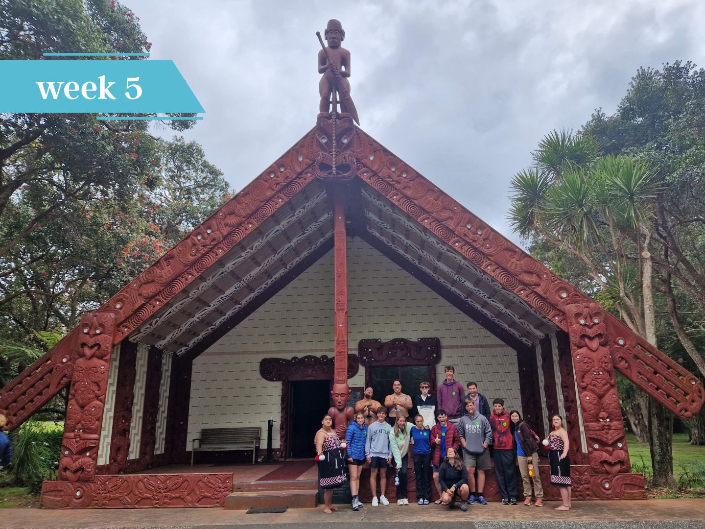 Group standing in front of a carved wooden meeting house